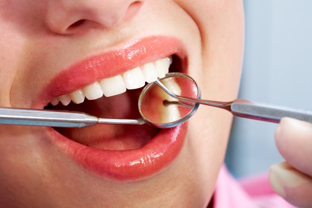 An image of a woman's teeth being checked by a dentist who practices minimally invasive dentistry.