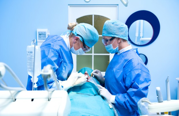 Two dentists preforming a dental implantation procedure, one of many dental surgeries.