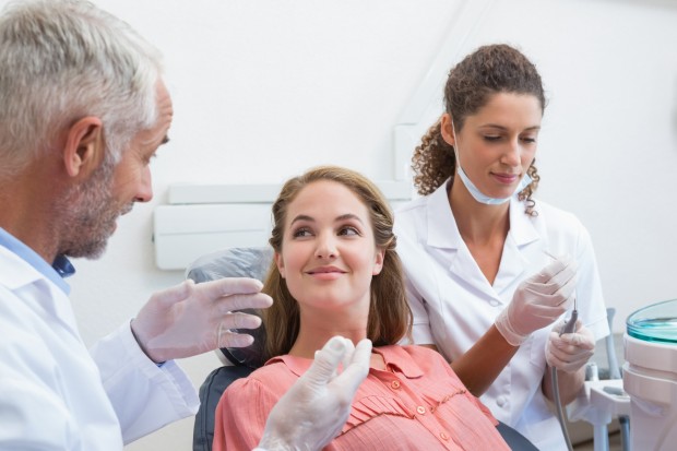 Dentist talking with patient while nurse prepares the tools at the dental clinic