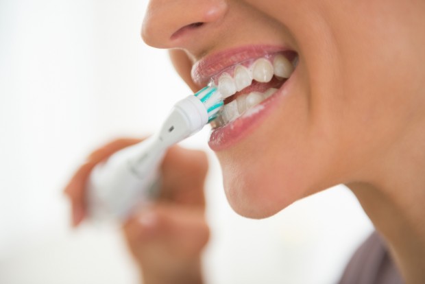 A closeup of a women brushing her teeth with an electric toothbrush.