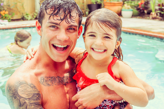 A young father and daughter enjoy a sunny day at their local swimming pool.